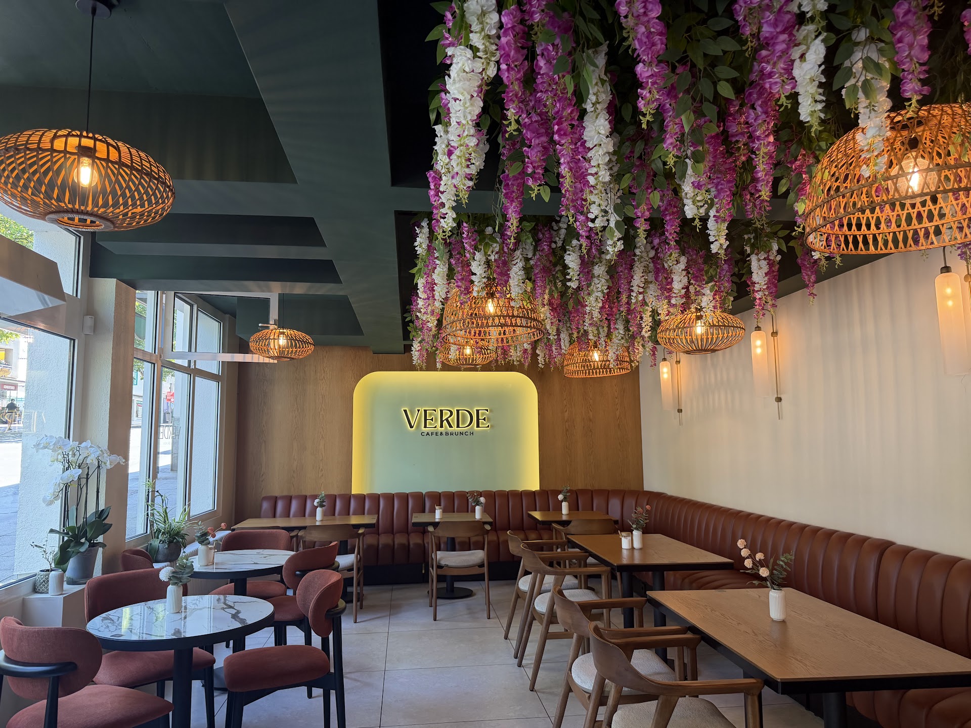 Innenraum des VERDE: grüne Decke, Rattanlampen, Blumeninstallation und leuchtendes VERDE-Logo